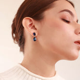 Close up of Azura Glow Drops, platinum-plated earrings with dark blue sapphire-like stones for an elegant, minimalistic look